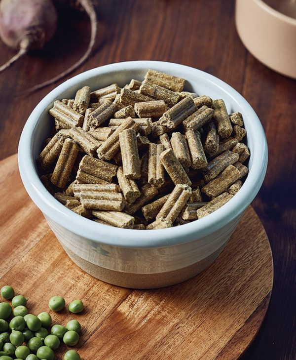 A rustic ceramic bowl on chopping board filled with James & Ella's cold-pressed natural dog food pellets