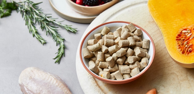 Bowl of James & Ella's freeze-dried chicken raw food on a chopping board surrounded by ingredients