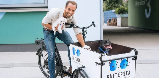 James Middleton holding fluffy white dog on Battersea babboe bike